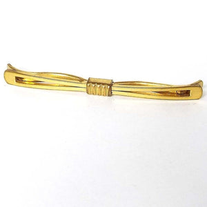 Angled front and top view of the 1930's Art deco collar clip bar. The metal is gold tone in color. The front bar is flared at the ends and has an open cut out middle area. The back bar has curves at the ends and there is a middle rectangle area with raised lines holding the front and back of the piece together.