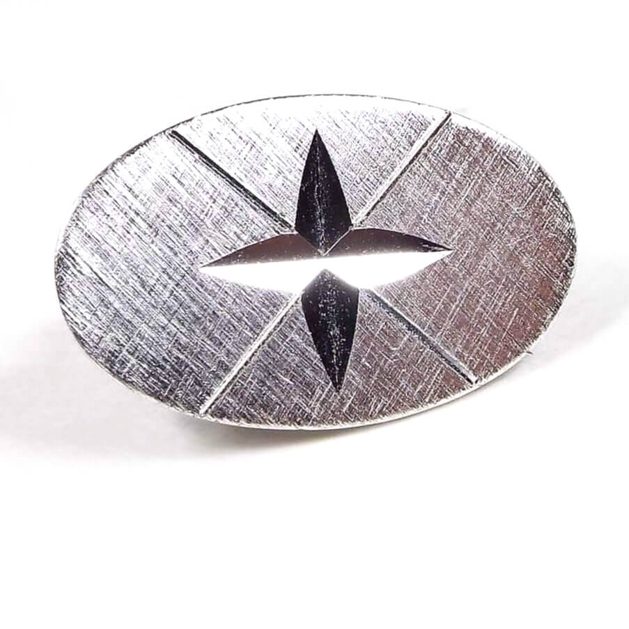 Front view of the Anson Mid Century vintage tie clip. It has a small oval shape with brushed matte silver tone color metal. The inside of the oval has a cut cross like star design with a thin etched X behind it. 
