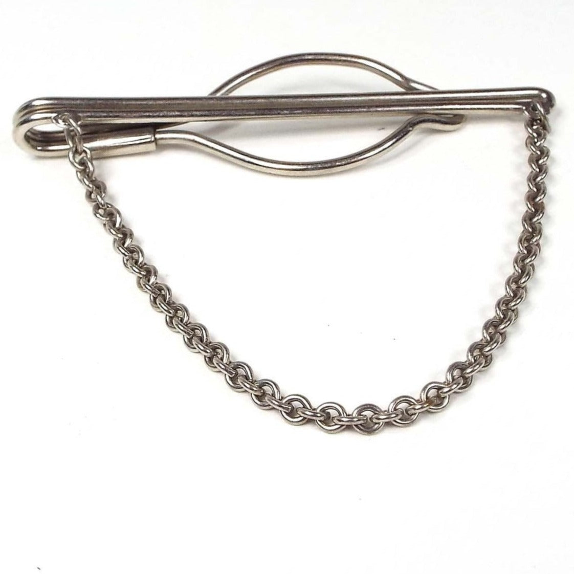 Front view of the 1940's Mid Century vintage tie bar chain. The metal is silver tone in color. The bar part is two rounded wires together on the front and curves around to the back where there is an open oval area. The tie slides between the two bar areas. Rolo chain hangs down from each side of the tie bar.