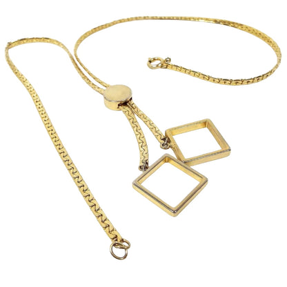 Top view of the retro vintage square pendant necklace. It is gold tone in color with C link chain. There is a round slide towards the bottom that can go up or down to adjust the length. At the bottom are two open square pendants. There is a round spring ring clasp at the end of the chain.