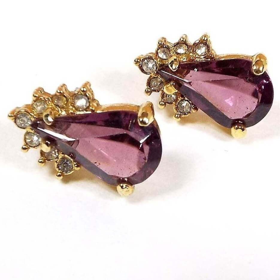Front view of the retro vintage rhinestone stud earrings. There are purple teardrop rhinestones on the bottom with an angled row of small clear round rhinestones at the top. All of the rhinestones are prong set. The metal is gold tone in color.
