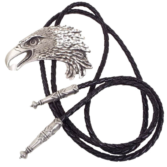 Front view of the retro vintage eagle bolo tie. The slide is a pewter detailed eagle's head with its mouth open. The cord ends are cone shaped with rounded and pointed ends. It has black dyed braided leather cord.