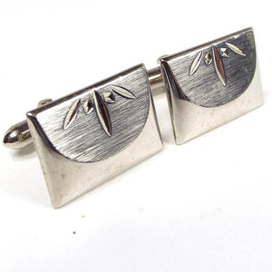 Angled front view of the retro vintage Swank cufflinks. The metal is gold tone in color. They are rectangle in shape with a half circle indented area that has a design etched towards the edge. Part of the rounded end levers on the back are showing in the photo.