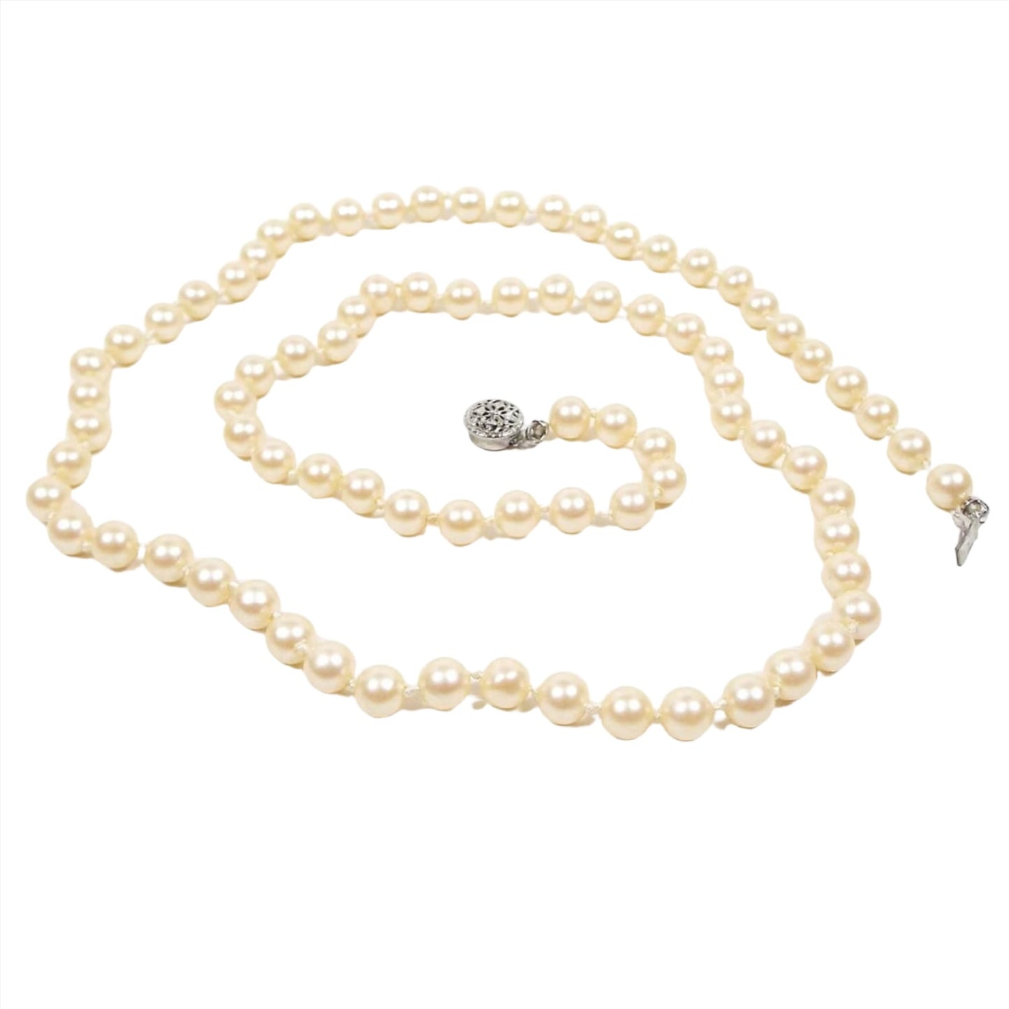 Top view of the Mid Century vintage faux pearl necklace. It is one strand of coated plastic round beads in an off white golden yellow color. The beads are have knots in between them. There is a silver tone filigree box clasp at the end.