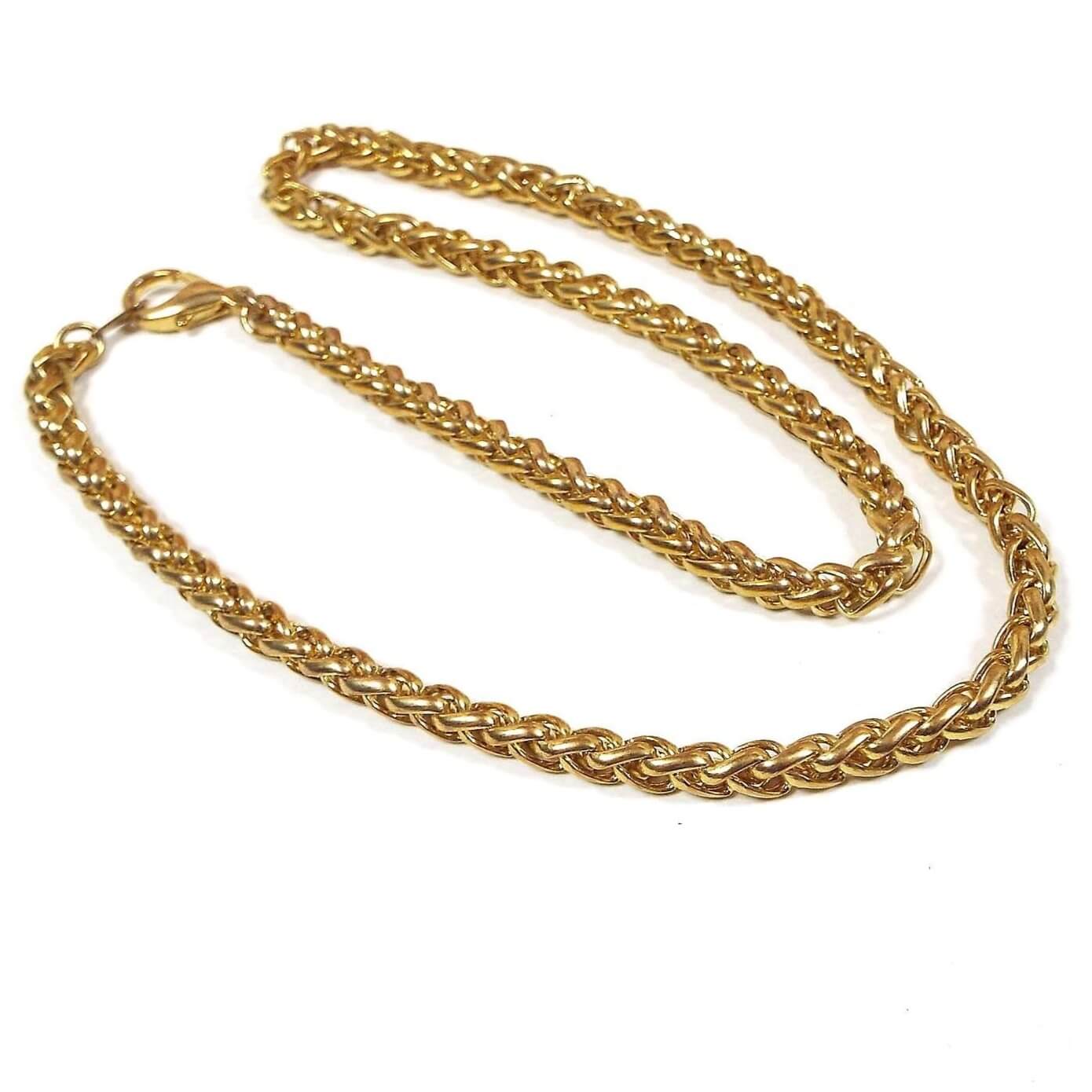 Top view of the 1990's retro vintage chain necklace. The metal is gold tone in color. It has a wider wheat chain design with a lobster claw clasp on the end.