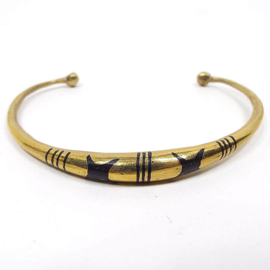 Front view of the retro vintage cuff bracelets. They are rounded brass color metal that tapers down to thin ends with a ball on the end. The middle top part has an indented and black painted design with three sets of lines that has two large X like shapes in between.