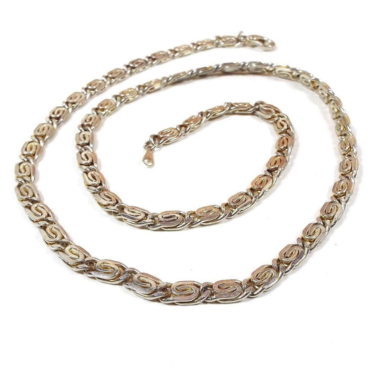 Top view of the retro vintage two tone chain necklace. The serpentine chain has larger S shaped links that are mostly silver tone in color with some gold tone on the edges in between the links. There is a lobster claw clasp at the end.