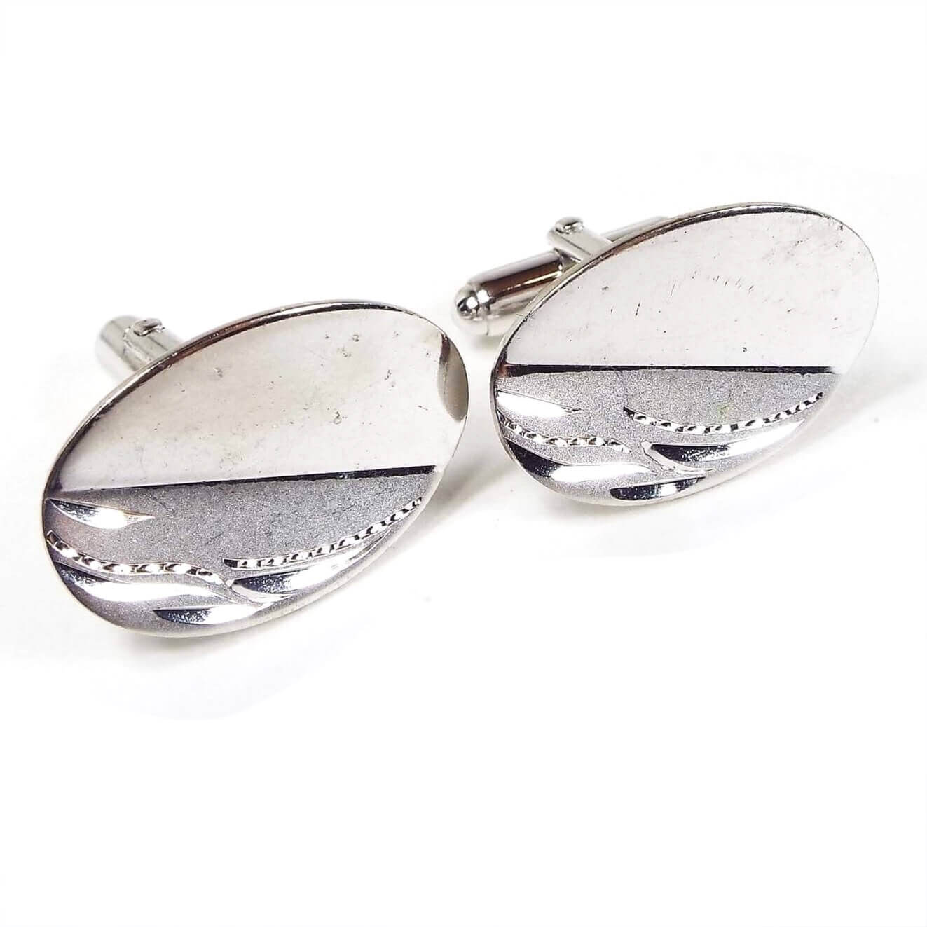Angled front view of the Mid Century vintage Anson sterling silver cufflinks. They are brighter silver in color and oval in shape. There have two diagonal sections on the oval with one being plain shiny silver and the other being matte silver with a shiny e