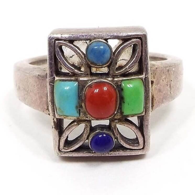 Angled top view of the retro vintage SE sterling silver multi gemstone ring. The middle has a red domed oval gemstone cab with a smaller sized blue domed cab on top and a dark blue domed cab below it. There is an aqua blue colored domed rectangle cab on one side and a green domed rectangle cab on the other. There are cut out marquis shaped areas at the corners of the rectangle. The sterling band is flared towards the top.
