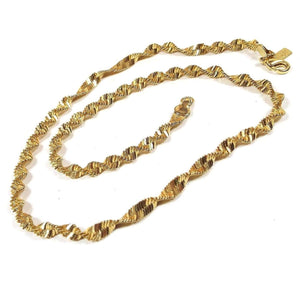 Top view of the retro vintage Lady Remington chain necklace. The metal is gold tone in color. The entire chain is a twisted herringbone link design with a lobster claw clasp at the end. There is a rectangle hang tag by the clasp with LR on it.