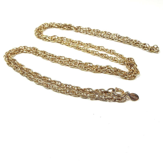 Top view of the retro 1970's Avon vintage chain necklace. Chain has oval shaped textured links with a twisted cable link style design. There is a round spring ring clasp at the end with an oval hang tag Marked Avon. The metal is gold tone in color.