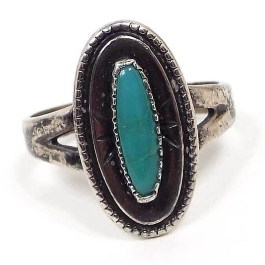 Front view of the Mid Century vintage Bell Trading Post turquoise ring. The top has a series of ovals. The edge of the main oval has dots around it, then there is a raised line oval, and finally in the middle is an oval bezel holding an oval turquoise gemstone cab. The sterling silver on the ring has a very darkened patina for a dark gray color.