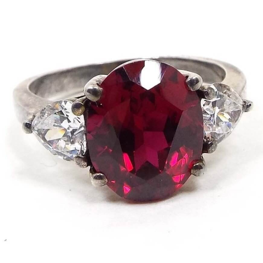 Angled front view of the retro vintage QVC Diamonique cubic zirconia multi stone ring. The top of the ring has a larger sized oval cubic zirconia in a deep red color. There is a triangle shaped trillion cut CZ stone on each side of the middle stone. The sterling silver is slightly darkened from age. All stones are prong set.