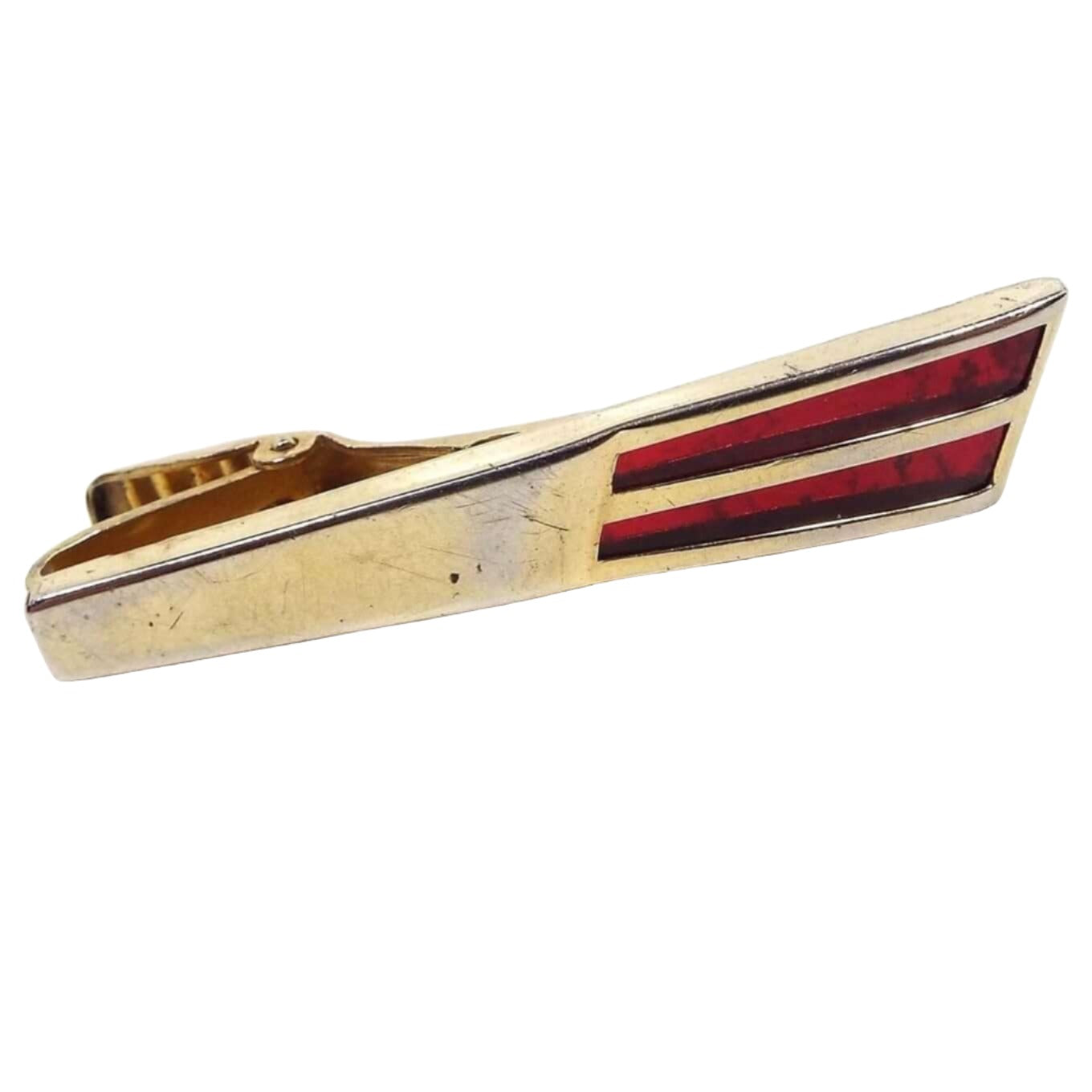 Front view of the Mid Century Anson vintage tie clip. It has a Modernist style flared gold tone metal bar with two flared stripes of inlaid lucite plastic at the end in a deep red color. There is some minor scruff scratching and an area in the middle that is slightly lighter on the metal from age. 