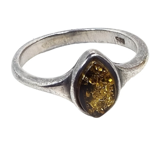 Angled front and side view of the retro vintage sterling silver amber ring. The top has a bezel set marquis shaped amber cab that's an olive green in color. The band at the top is slightly flared at the bezel. The 925 marking can be seen on the inside of the band. The sterling is matte and slightly darkened in color from age.
