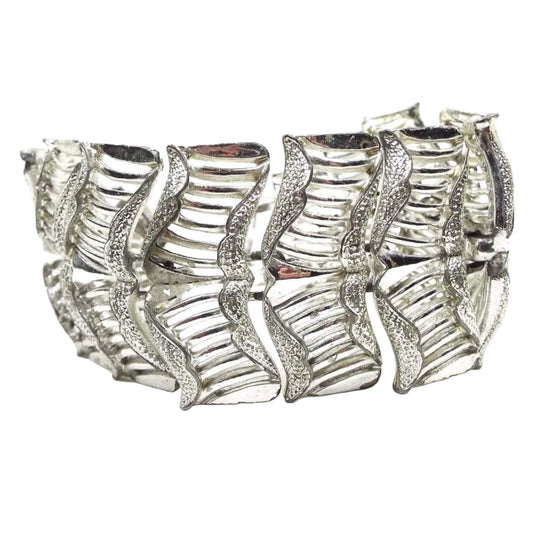 Front view of the top of the Mid Century vintage Coro panel link bracelet. It is silver tone in color and has wide links with wavy textured curled edges and a cut out line design. 