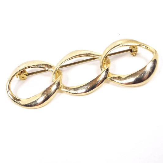 Front view of the retro vintage brooch pin. The metal is gold tone in color. It has a large open curb link design with three oval links. The long pin and safety catch clasp can be seen on the back.