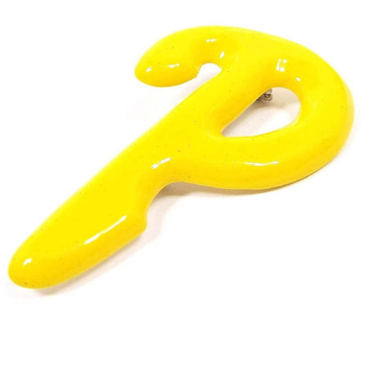 Angled front view of the retro vintage letter brooch pin. It is bright yellow plastic in the shape of a block initial P that has a curve at the top.