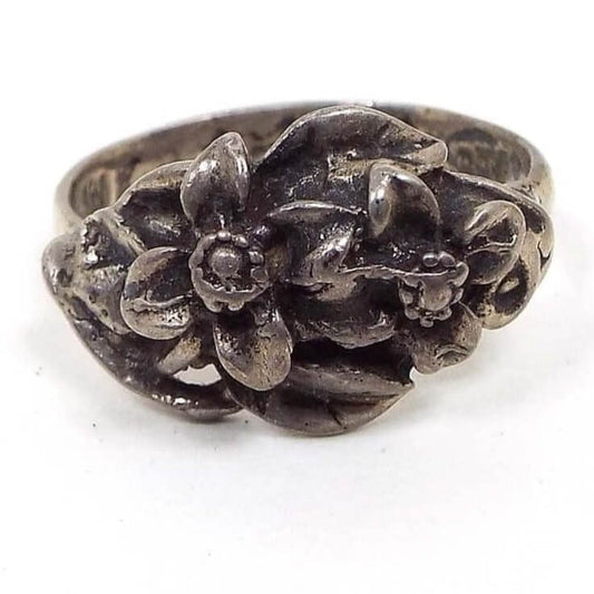 Front view of the retro vintage Mexican CTP sterling silver ring. It has a nice Boho floral design with two raised 3D style flowers that have four petals each. The rest of the top of the ring has raised leaves. The sterling is very darkened from age for a gray in color.
