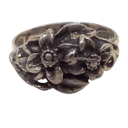 Front view of the retro vintage Mexican CTP sterling silver ring. It has a nice Boho floral design with two raised 3D style flowers that have four petals each. The rest of the top of the ring has raised leaves. The sterling is very darkened from age for a gray in color.