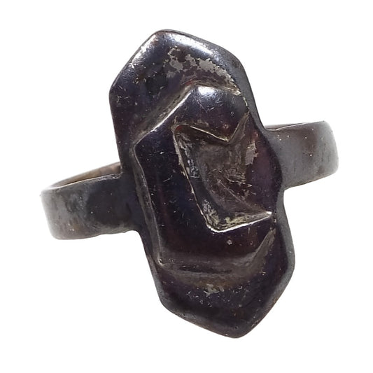 Front view of the 1950's Mid Century vintage adjustable signet Ring. The ring is very darkened from age for a dark gray in color. There is a hexagon shape in the middle that is elongated with pointed ends. A block letter initial C is on the front of the hexagon. 