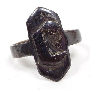 Front view of the 1950's Mid Century vintage adjustable signet Ring. The ring is very darkened from age for a dark gray in color. There is a hexagon shape in the middle that is elongated with pointed ends. A block letter initial C is on the front of the hexagon. 