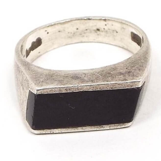 Angled front and side view of the retro vintage sterling silver onyx gemstone ring. The top part has a long channel set horizontal rectangle shape black onyx cab. The sides of the band are flared at the top. The sterling is slightly darkened from age. The 925 marking can be seen on the inside of the band. 