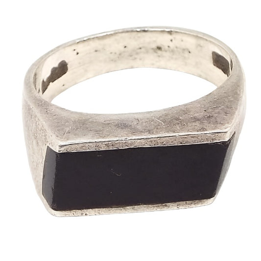 Angled front and side view of the retro vintage sterling silver onyx gemstone ring. The top part has a long channel set horizontal rectangle shape black onyx cab. The sides of the band are flared at the top. The sterling is slightly darkened from age. The 925 marking can be seen on the inside of the band. 
