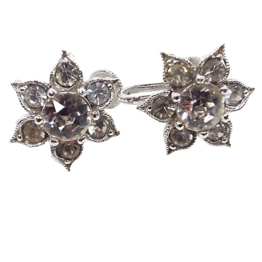 Front view of the 1950's Mid Century vintage rhinestone screw back earrings. They have a metal silver tone color flower like design with pointed end petals. Each petal has a round clear rhinestone and there is a larger round clear rhinestone in the middle of the earrings. The middle rhinestone is prong set and the others are set with adhesive. 