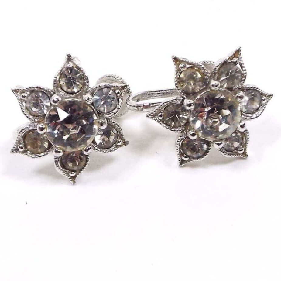 Front view of the 1950's Mid Century vintage rhinestone screw back earrings. They have a metal silver tone color flower like design with pointed end petals. Each petal has a round clear rhinestone and there is a larger round clear rhinestone in the middle of the earrings. The middle rhinestone is prong set and the others are set with adhesive. 