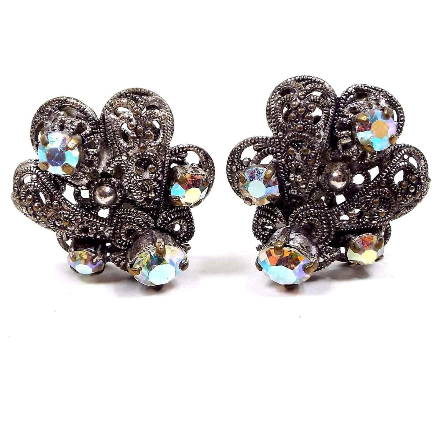 Front view of the Mid Century vintage German AB rhinestone clip on earrings. The metal is darkened silver tone color from age. It has a filigree sort of peacock feather flare style design with rounded ends and every other part has a small round AB clear rhinestone on it. The rhinestones are prong set and have a coating to give them a multi color shimmer when you move around.