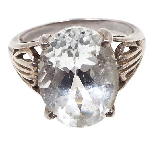 Angled top view of the retro vintage SCBS sterling silver white topaz solitaire statement ring. The top has a large prong set oval white topaz that is almost clear in color. The sterling band flares a the top and has a split band design with a cut out pattern in the middle. 